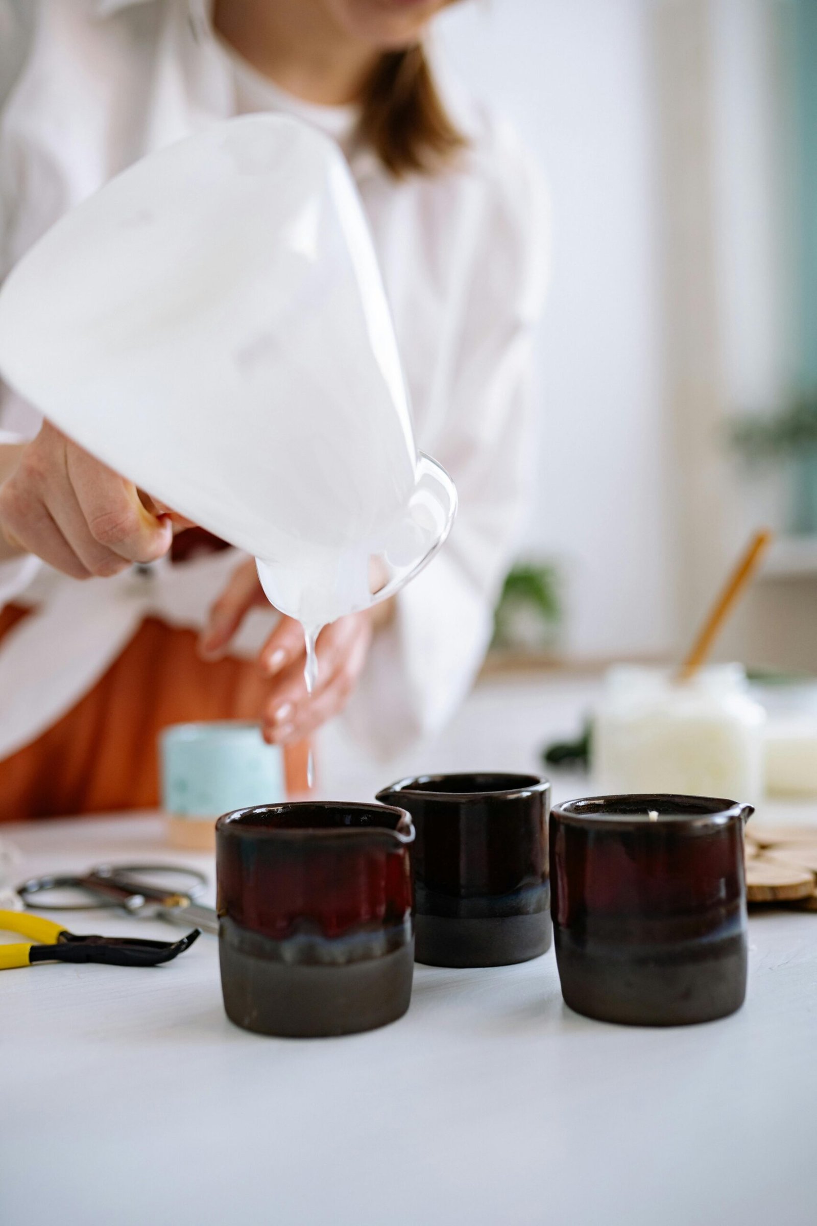 Person pouring candle wax into dark glass jars, showcasing the craft of candle making.