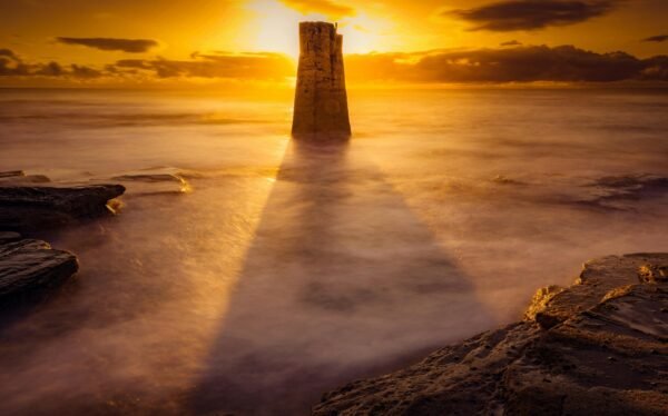 Majestic sunset over the ocean with a dramatic silhouette and sunrays casting shadows.
