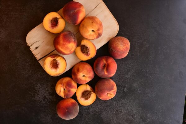 Top-down view of fresh and juicy peaches on a wooden cutting board with dark background.