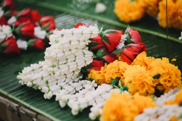 Colorful flower garlands displayed on a banana leaf in a Bangkok street market.