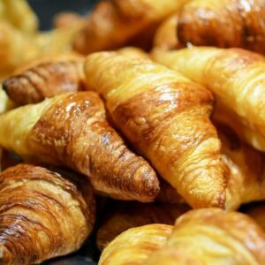 A stack of golden, freshly baked croissants showcasing flaky layers in a bakery setting.