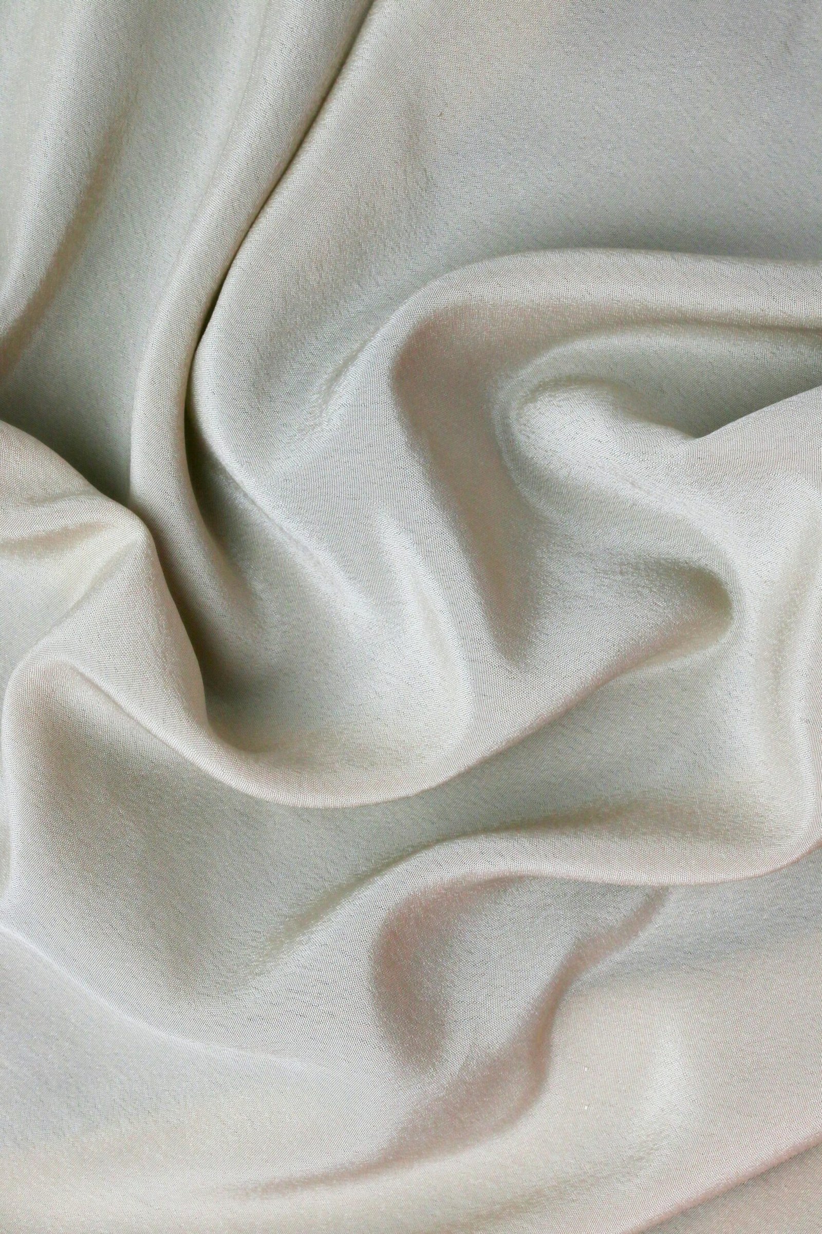 Detailed close-up of smooth white satin fabric with rippled texture, showcasing elegance and luxury.